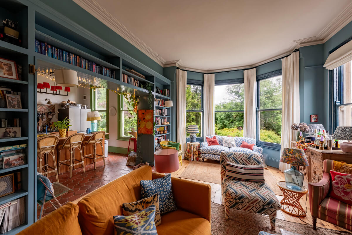 open-plan living room kitchen blue walls bookshelves bay window